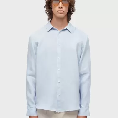 Camisa azul clara de manga comprida em modelo masculino com calças bege e óculos de sol