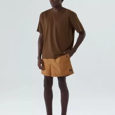 Homem com t-shirt castanha, calções curtos mostarda e sapatos castanhos com biqueira branca