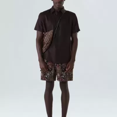 Homem com camisa castanha, calções florais e bolsa castanha