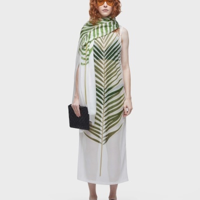 modelo com vestido branco com folha verde, xale, óculos de sol laranja e sandálias pretas