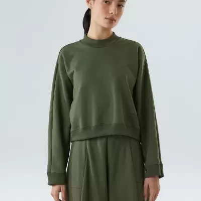 Pessoa com conjunto verde-oliva de camisola e calças sobre fundo cinzento claro