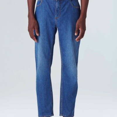 Homem a usar calças de ganga azuis retas e sapatos brancos em fundo claro