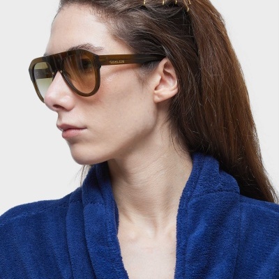 Óculos de sol castanhos com lentes escuras usados por mulher com cabelo preso e roupão azul