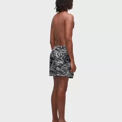 Homem vestido com calções de banho pretos e brancos, sandálias pretas, visto de costas