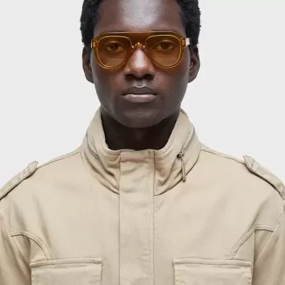 Homem com óculos de sol âmbar e casaco bege em fundo branco