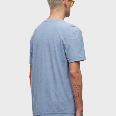 Homem de costas com t-shirt azul clara e calças azuis claras, cabelos loiros e óculos amarelos