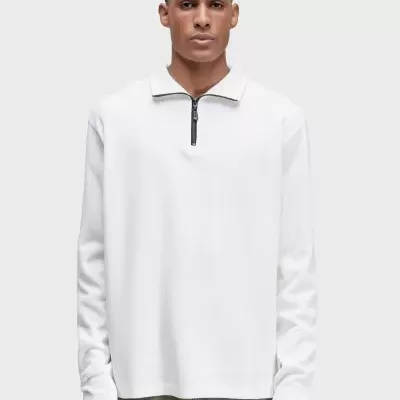 Homem a usar polo branco de manga comprida com fecho no decote