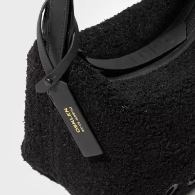 Bolsa preta felpuda com alça de couro e etiqueta OSKLEN