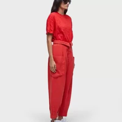 mulher com t-shirt vermelha, calças largas coral e ténis brancos num fundo cinza