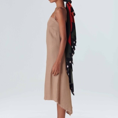 Mulher vestindo vestido bege de alças finas, sandálias brancas e lenço colorido na cabeça de perfil