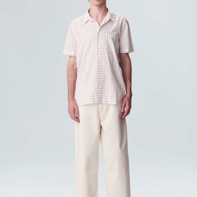 Homem com camisa branca de manga curta com padrão de grelha e calças largas brancas