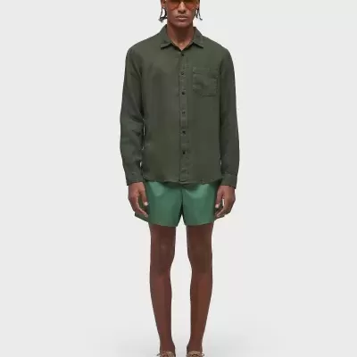 Homem com camisa verde escura, calções verdes claros, sapatos bege e óculos escuros laranja