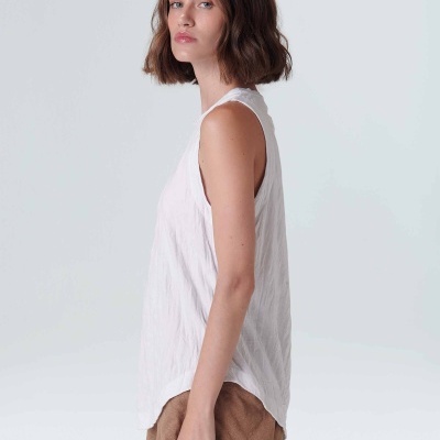 Mulher com top branco sem mangas e bermuda castanha de perfil