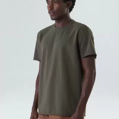 Homem a usar camiseta verde-oliva e calções castanhos numa parede branca