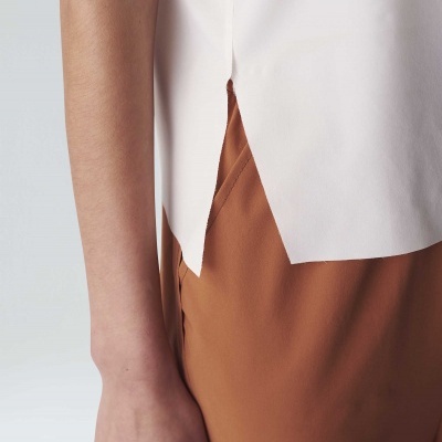 Braço esquerdo de uma pessoa com blusa branca sem mangas e saia/calça castanha