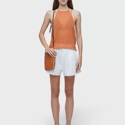 Mulher com top laranja, calções brancos, sandálias pretas, óculos de sol castanhos e bolsa laranja