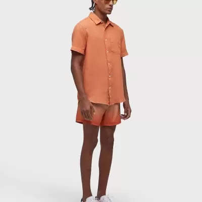 Homem com camisa de manga curta e calções laranja e sapatilhas brancas com sola laranja.