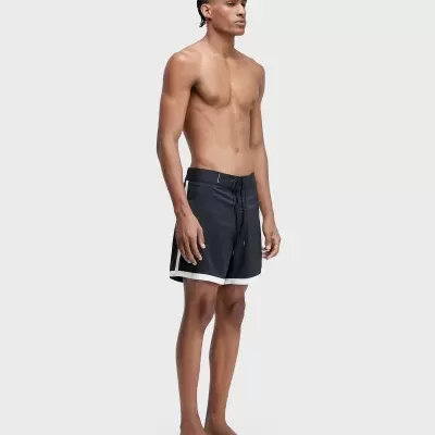 Homem com calções de banho pretos com detalhes brancos, posando em fundo cinza claro