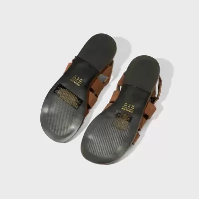 Sandálias castanhas vistas por baixo com sola preta e etiquetas amarelas