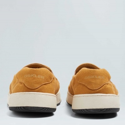 Par de sapatilhas castanhas de lona com sola branca em fundo cinzento.