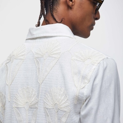 Pessoa de costas a usar camisa branca com bordados florais em creme