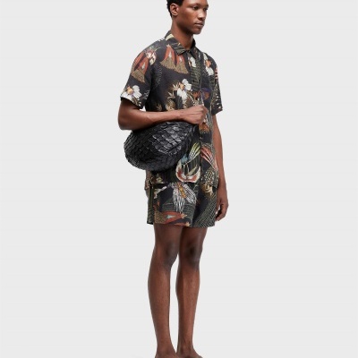 Homem com conjunto floral escuro e mala preta texturada