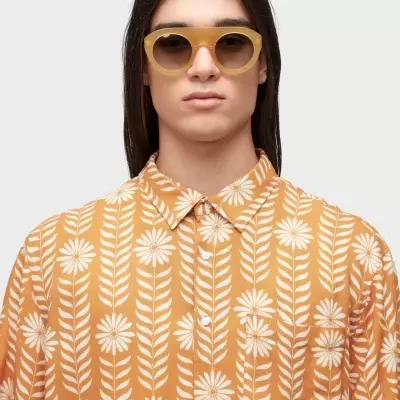 Pessoa com camisa floral laranja e branca e óculos de sol bege