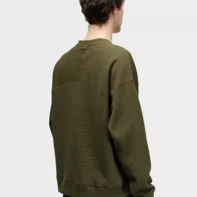 Casaco verde em malha texturada visto de costas com fundo cinza claro