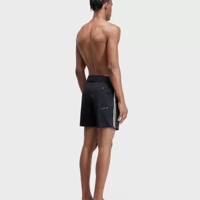 Homem sem camisa de costas com calções de banho pretos com riscas brancas e bolso traseiro