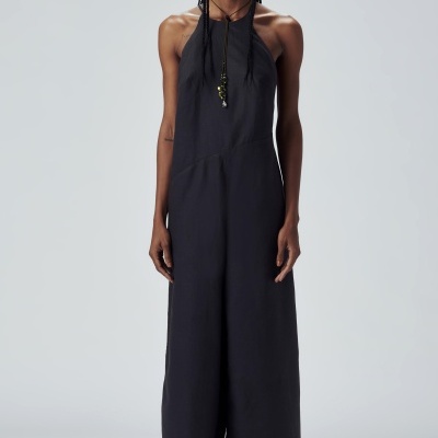 Mulher a usar macacão preto sem mangas com decote halter e sandálias pretas