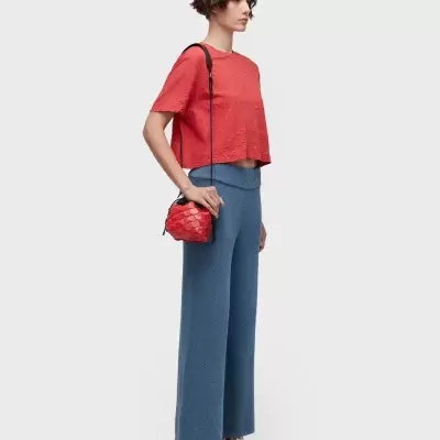 Mulher com t-shirt vermelha texturada, calças azuis largas, sapatilhas brancas com riscas, e mala vermelha pequena