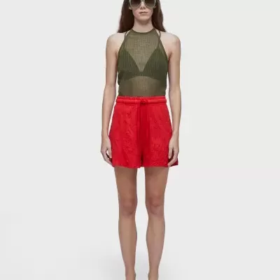 Mulher com top verde, calções vermelhos e óculos de sol em fundo branco