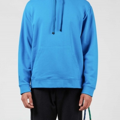 Camisola azul com capuz e bolso frontal, usada com calças pretas e corda colorida pendurada