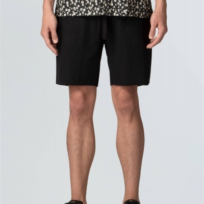 Calções pretos simples com cordão na cintura usados por homem com camisa preta de flores e sapatilhas pretas