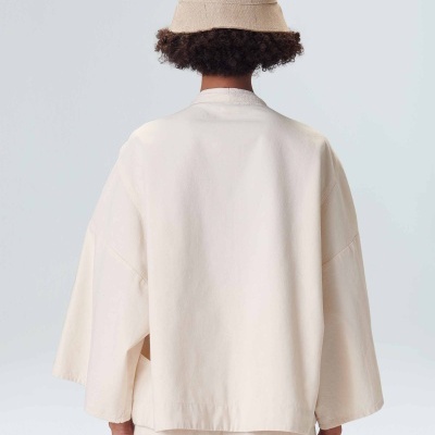 Pessoa de costas com casaco creme de manga larga, calças creme e chapéu de balde bege de malha.