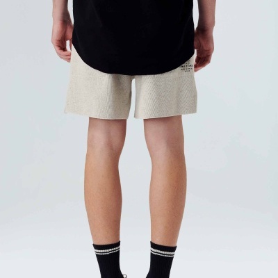 Vista traseira de shorts bege texturizados com etiqueta, t-shirt preta, meias pretas às riscas e sapatilhas brancas e pretas.