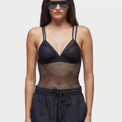 Mulher de cabelo comprido usa óculos escuros, body preto de malha e calças pretas com cordão