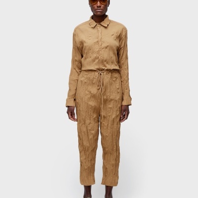 Conjunto feminino castanho texturizado com camisa de gola e calças com cordão, calçado com sapatilhas bege.