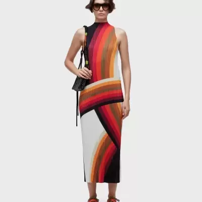 Vestido comprido de malha com riscas curvas coloridas, ténis castanhos com atacadores vermelhos, óculos escuros e bolsa preta.