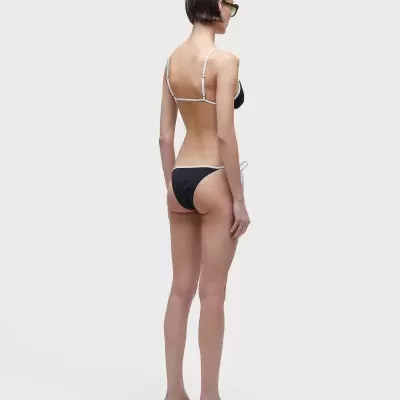 Mulher com biquíni preto e branco vista de costas, sobre fundo branco