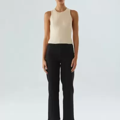 Mulher com camisa bege sem mangas, calças pretas, sapatos castanhos e óculos de sol amarelos