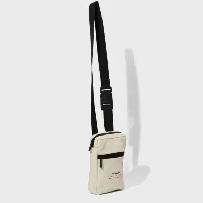 Mala pequena de ombro bege com alça preta e bolso frontal com texto.