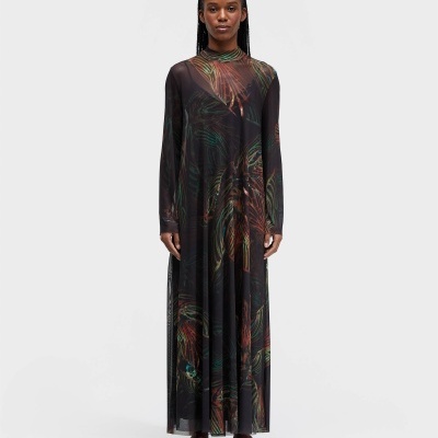 Vestido comprido transparente com padrão de folhas coloridas, usado por mulher com sandálias castanhas.