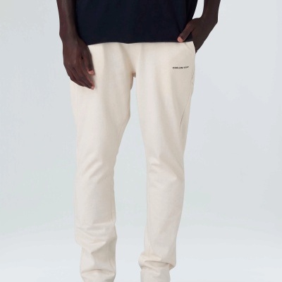 Calças desportivas creme com texto perto do bolso direito.