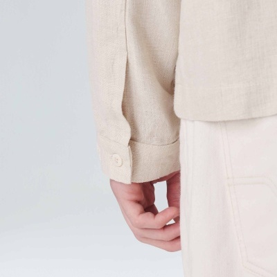 Manga de camisa bege claro com botão e calça clara num fundo branco