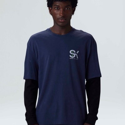 Homem vestido com t-shirt azul escura e camisa preta de mangas compridas, com logotipo 'S| SINCE 1995' na t-shirt