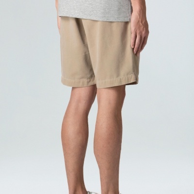 Homem de costas com bermudas bege, t-shirt cinzenta e ténis brancos com pormenores castanhos e pretos.