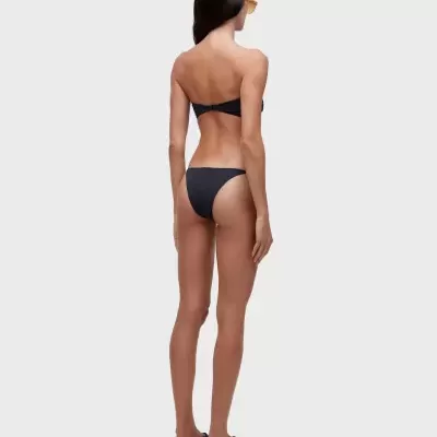 Mulher de costas a usar biquíni preto e sandálias pretas com sola clara