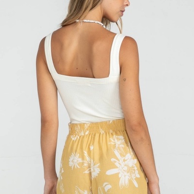 Calções amarelos com estampa branca de flores, vistos de costas, usados com top branco largo