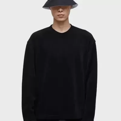 Pessoa com chapéu bob preto, camisa preta e calças pretas perante fundo cinza